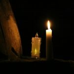 Two lit candles in darkness with a dark background.