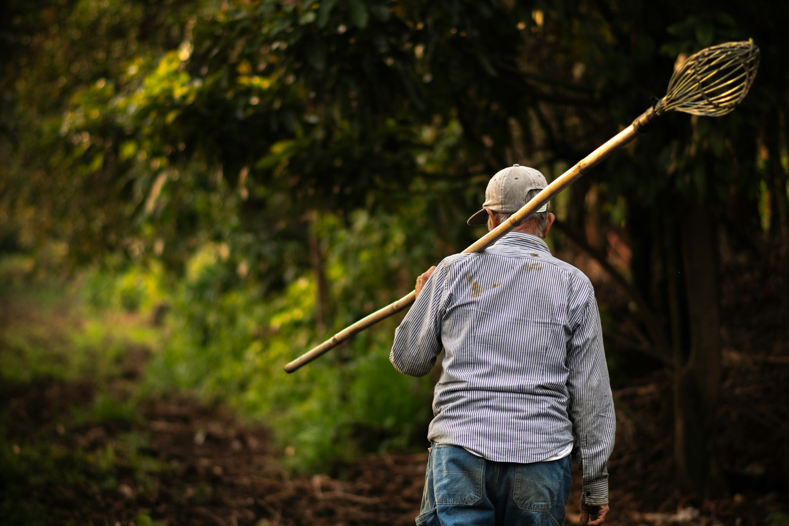 a man with a broom on his back walking down a dirt road
